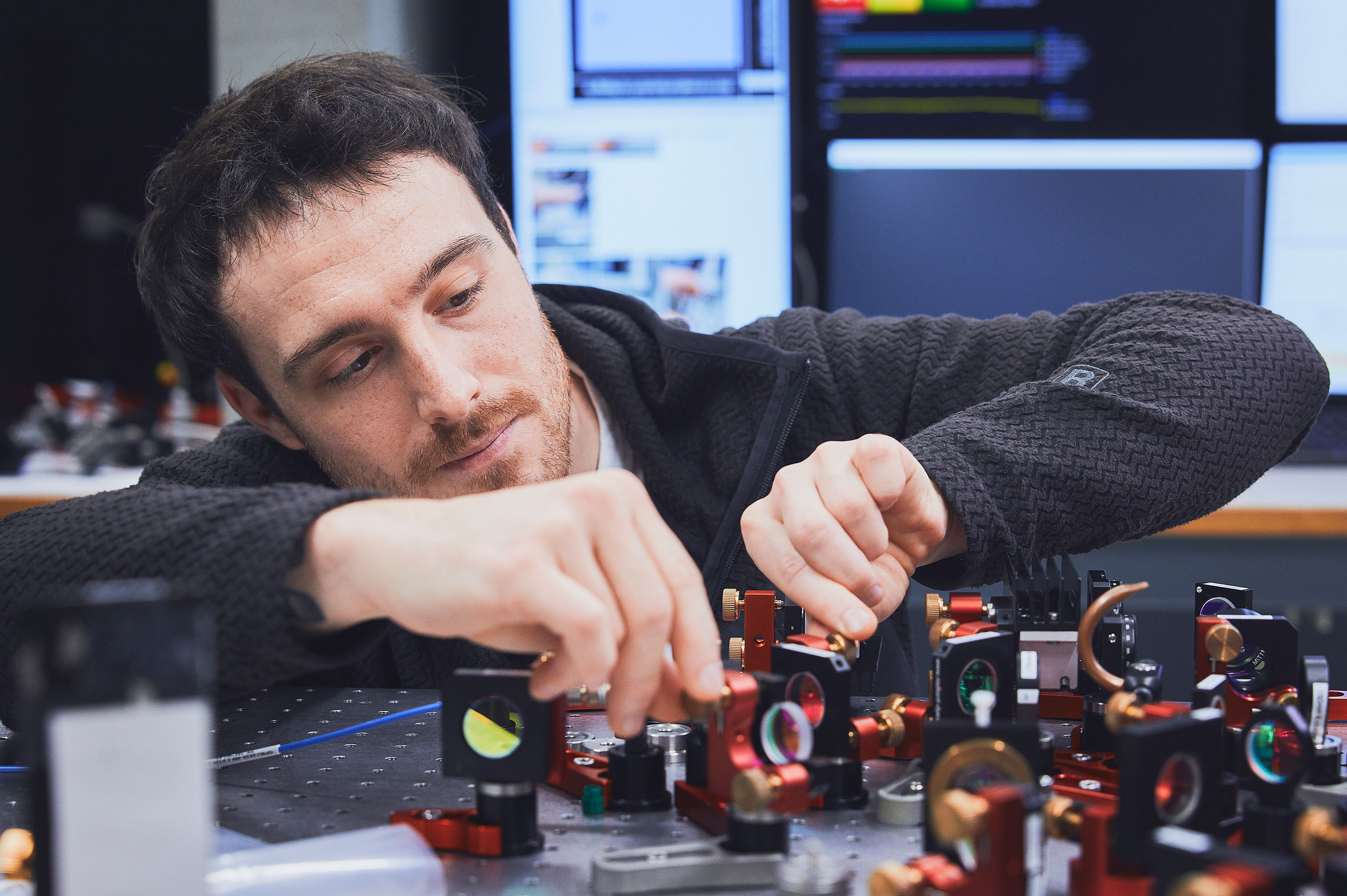 A man turning the knobs of an optical elements' mount on an optical table